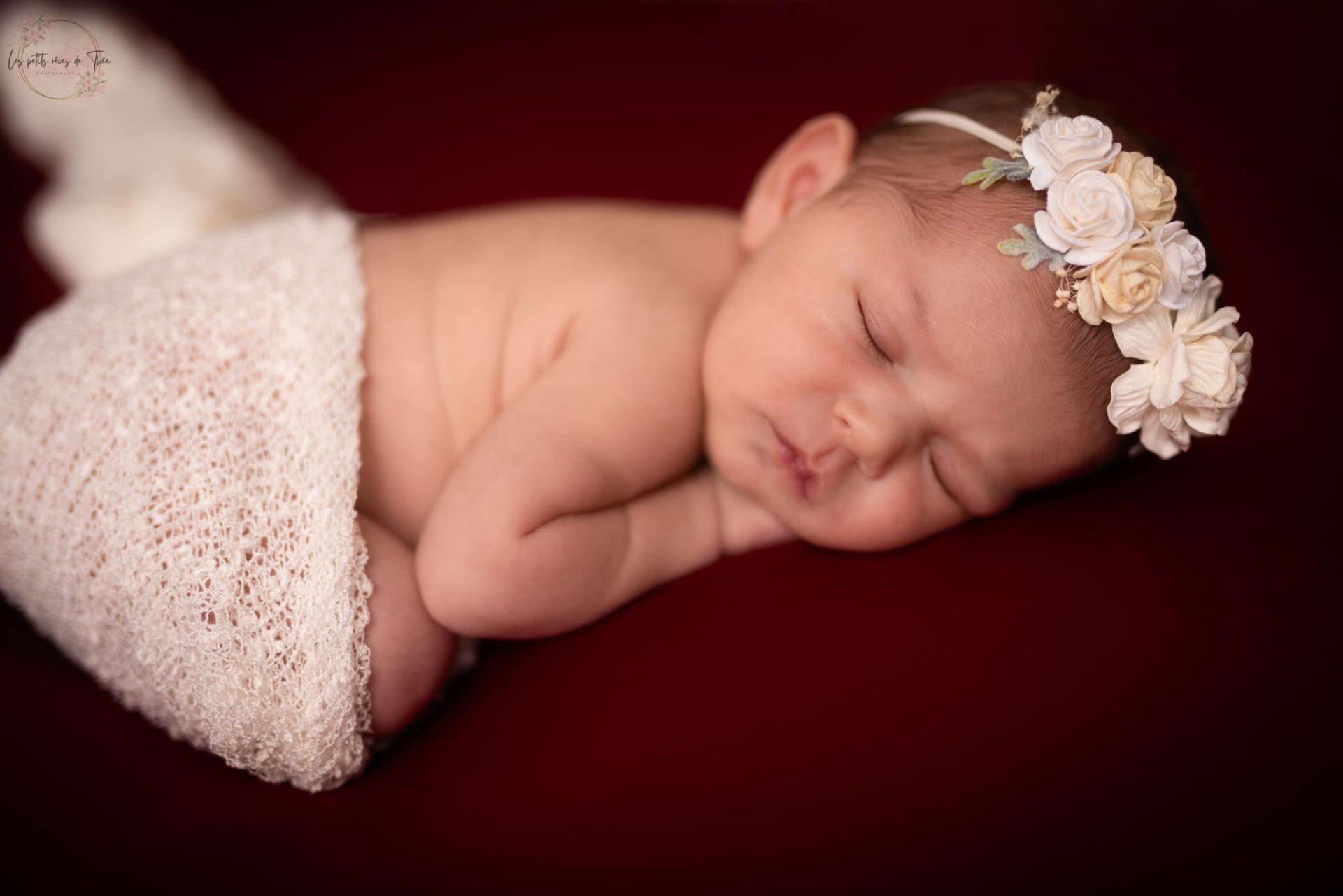 bébé qui dort avec une couronne de fleur sur fond rouge